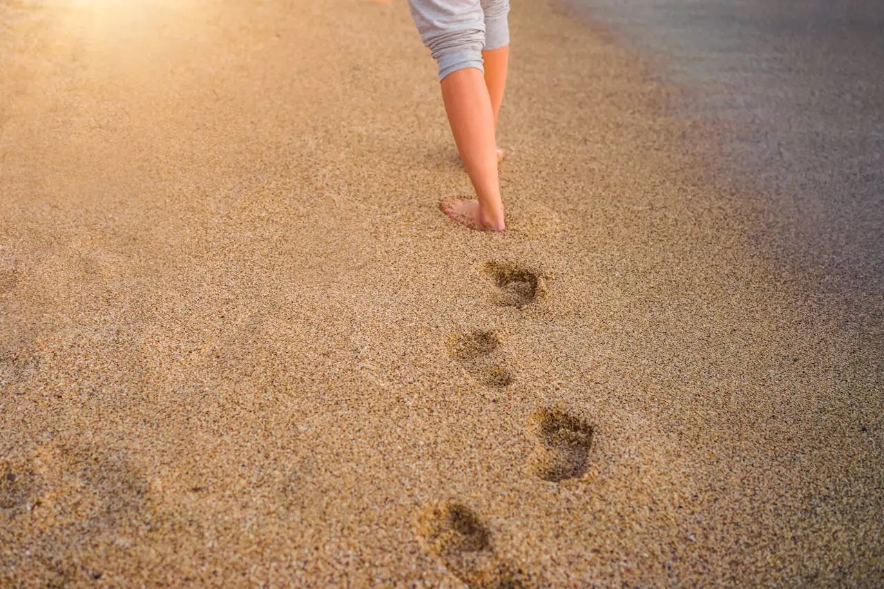 Barfüßige Person hinterlässt Fußspuren im Sand – achtsames Gehen und Loslassen beim Retreat